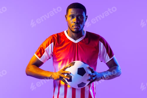 Vista previa: Portrait of african american male soccer player with football over neon pink lighting