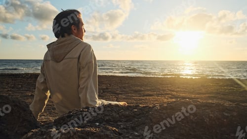 Preview: Man on a beach is looking distance during beautiful summer sunset.