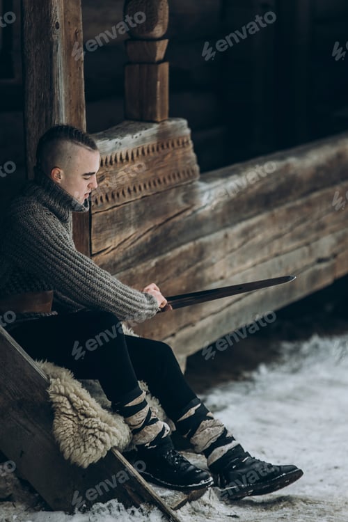 Preview: Portrait of strong viking warrior sharpening his sword, scandinavian viking cosplay