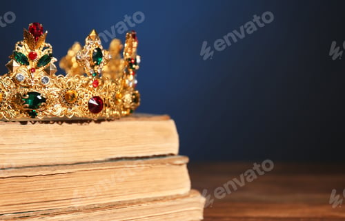 Preview: Beautiful golden crown on old books against dark blue background, space for text. Fantasy item