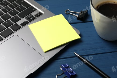 Preview: Laptop with sticky note, pen, paper clips and coffee on blue wooden table, closeup