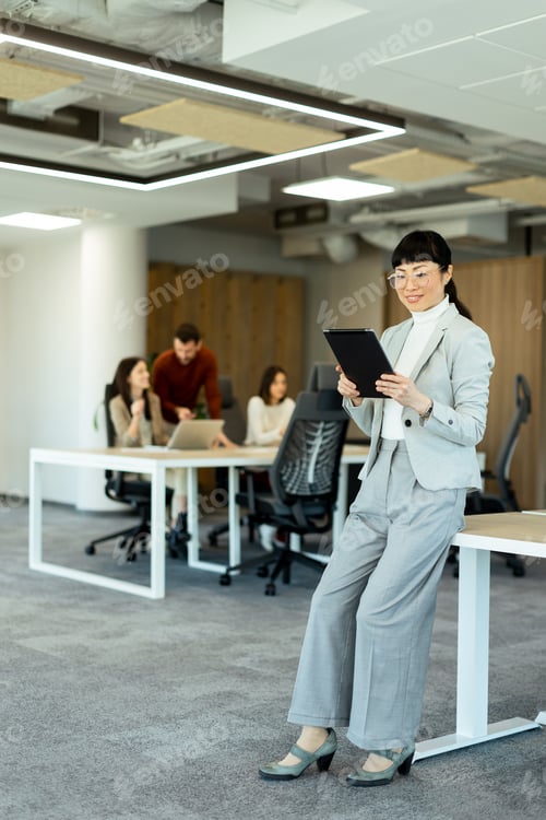 Preview: Asian businesswoman engaged with a tablet in a modern office environment during a team meeting