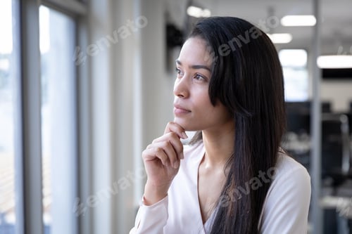 Vista previa: Thoughtful businesswoman looking out of a window while her hand on her chin at modern office