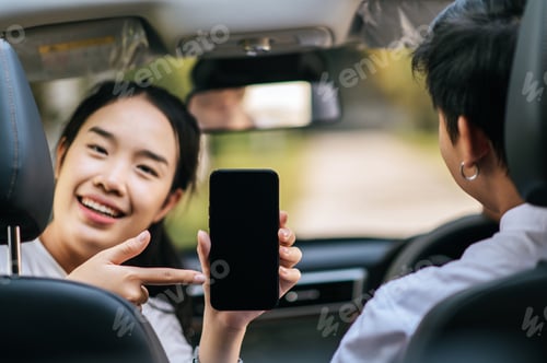 Preview: a woman and a man sitting in a car and looking at a cell phone