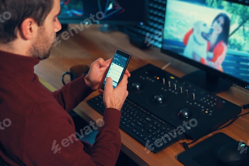 Preview: Young man working in the studio using a smartphone and computer.