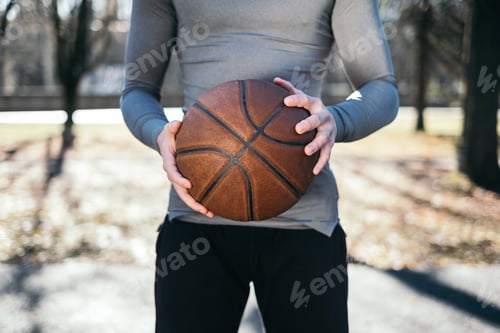 Preview: Man Holds Basketball Outdoors on Sunny Day