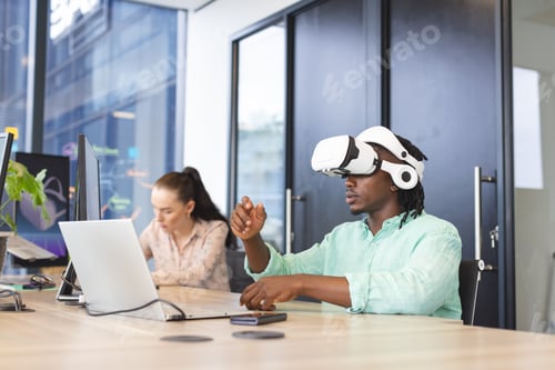 Preview: African American man wearing VR headset, Caucasian woman using laptop at work in a modern business o