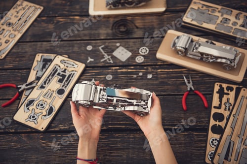Preview: Careful Young Lady Sitting At The Table Covered With Details Of The Constructor And Holding Metal