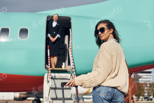 Preview: Young female passanger in casual clothes is outdoors near the plane