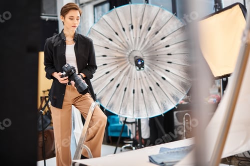 Preview: gorgeous focused female photographer holding camera and prepearing to take photos in her studio