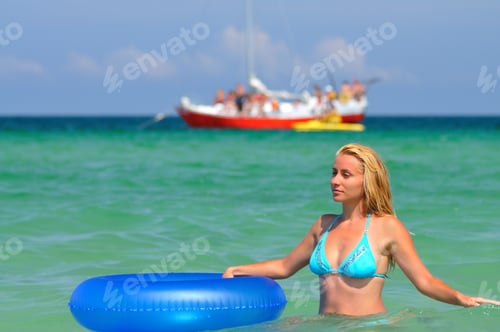Preview: Young blond woman in blue bikini riding on swimming circle in sea and smiling