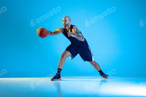 Preview: Young basketball player training isolated on blue studio background in neon light
