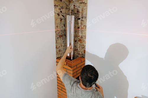 Preview: A young man makes brickwork on the chimney of a fireplace.