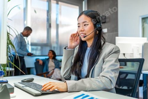 Preview: Asian operator working in coworking office with headset and keyboard