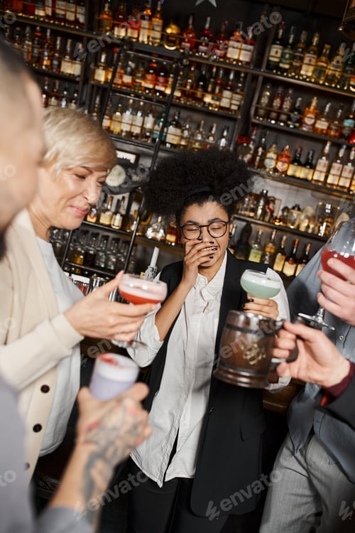 Preview: excited african american woman laughing with closed eyes near team of colleagues with drinks in bar