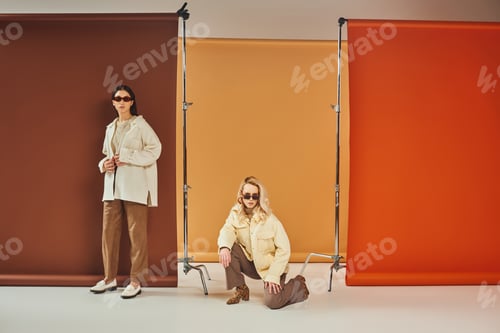 Preview: interracial models in sunglasses and autumn outerwear posing on colorful backdrop, fall colors