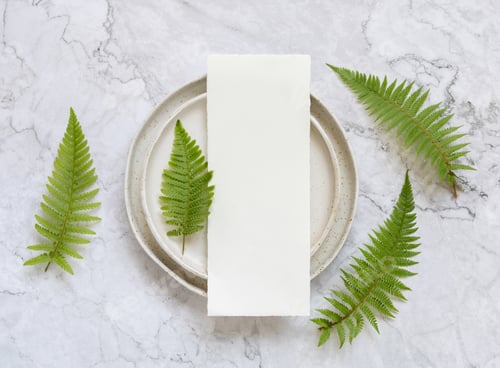 Preview: Blank paper card on plate on marble table with fern leaves