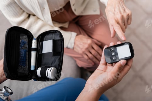 Preview: top view of cropped nurse holding diabetes kit and glucometer near senior woman