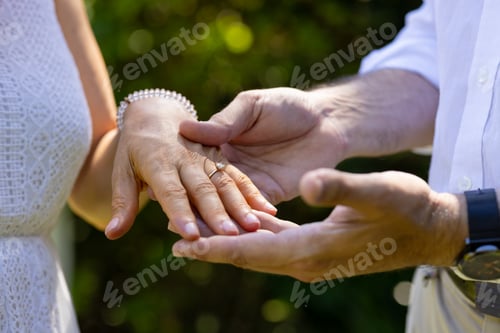 Preview: Showing engagement ring, groom holding bride's hand at outdoor wedding