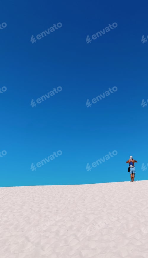 Preview: Vertical shot of a tan male on a pristine white sand beach under a brilliant blue sky