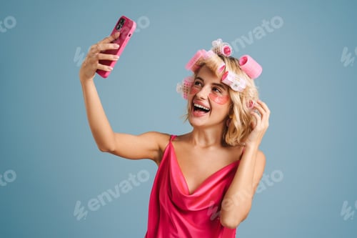 Preview: Young woman with curlers taking selfie photo on cellphone