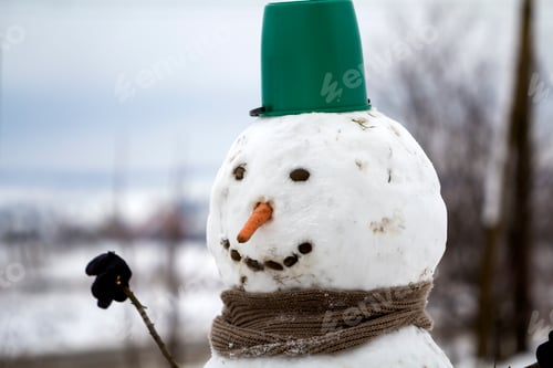 Preview: Close-up of big funny primitive smiling snowman head with carrot nose, black stone eyes and teeth in