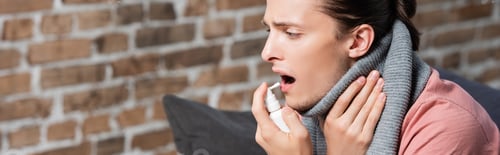 Preview: website header of ill young man in warm scarf touching neck while using throat spray