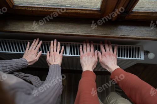 Preview: Top view of man and woman warm hands by placing on radiator due to sharp onset of cold weather