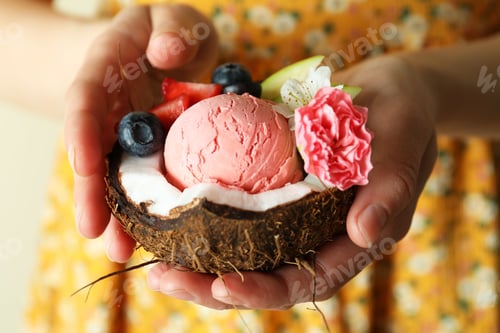 Preview: Woman holds coconut with fruit ice cream, close up