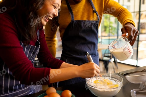 Preview: Happy diverse couple baking christmas cookies mixing dough in kitchen