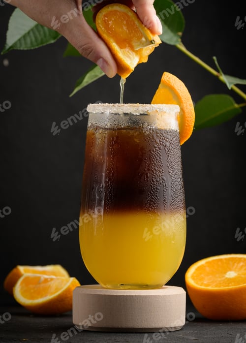 Preview: Iced coffee with orange juice in a transparent glass, a woman's hand squeezes an orange slice