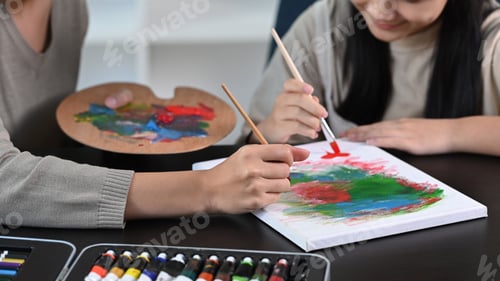 Preview: Smiling asian girl having fun painting with her mother at home.
