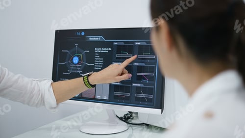 Preview: Doctor gesturing towards a display monitor with her finger showing the results to the patient