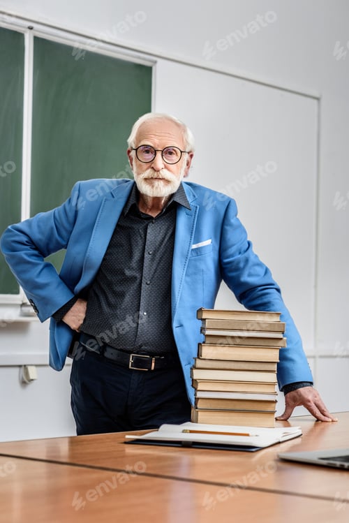 Preview: grey hair professor standing near stack of books