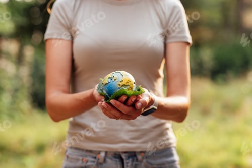 Preview: Young woman holding small planet in hands against spring or summer green eco background.