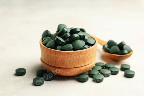 Preview: Wooden bowl and spoon with spirulina pills on white textured background