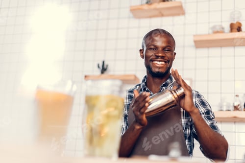 Preview: smiling handsome african american bartender making cocktail in shaker on bar counter