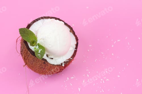Preview: Vanilla ice cream balls in fresh coconut halves, decorated with mint leaves on a pink background