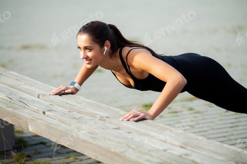 Preview: Athletic woman standing in plank position outdoors at sunset