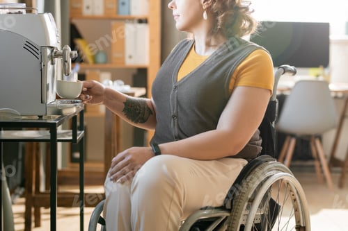 Preview: Young businesswoman in wheelchair making coffee at break in office environment