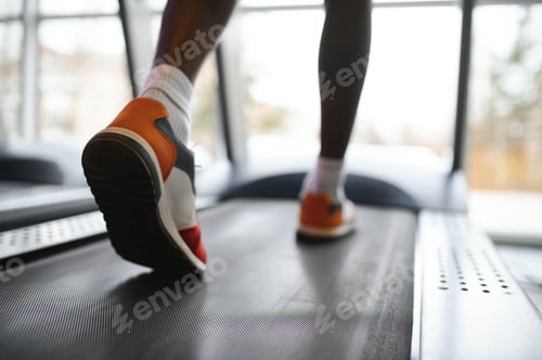 Preview: Back view of unrecognizable male legs running on treadmill in gym.