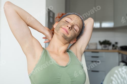 Preview: portrait young attractive positive woman in morning in cosmetic mask, in kitchen, having breakfast