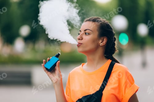 Preview: Pretty young hipster woman vape ecig, vaping device at the sunset. Toned image.