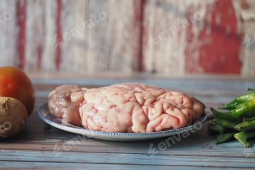 Preview: A animal brain placed on a silver plate next to assorted vegetables