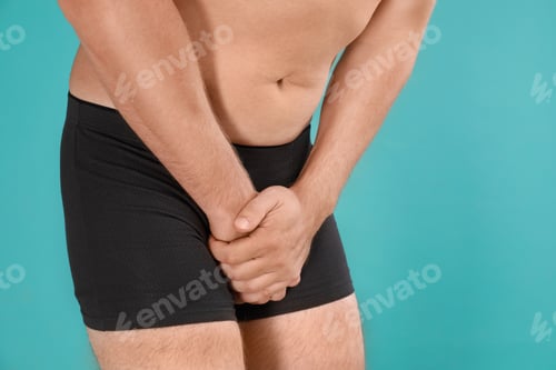 Preview: Man suffering from pain on turquoise background, closeup. Urology problems