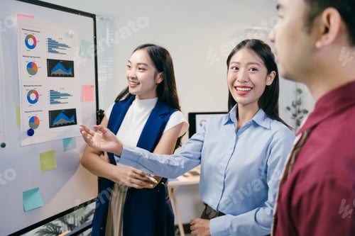 Preview: Smiling asian businesswomen presenting business performance report using whiteboard charts, explaini