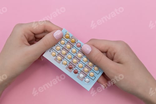 Preview: Female hands holding a blister pack with oral contraceptives on a pink background