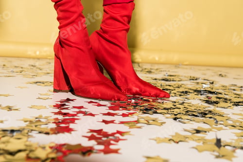 Preview: Cropped view of woman in red high-heeled shoes standing on confetti on yellow background
