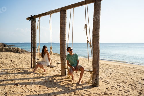 Preview: Tourists relaxing on tropical beach swings at sunset