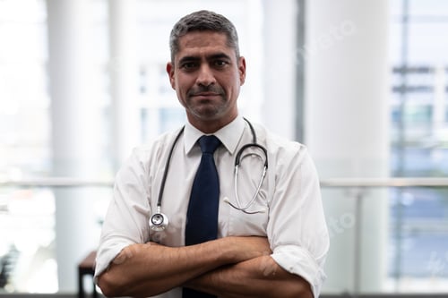 Preview: Portrait of smiling mature Caucasian male doctor with arms crossed looking at camera in clinic
